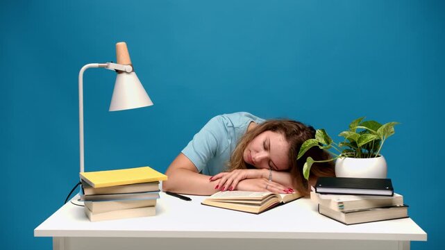 Tired female student sleeping on a book at her desk after studying for an exam. Exhaustion and overwork concept