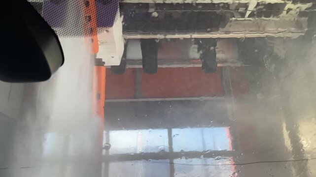 inside car view at the end of an automatic car wash,cleaner windshield with scattered droplets and thin rinse streams,soft reflections and motion,vehicle care,maintenance and cleanliness concept