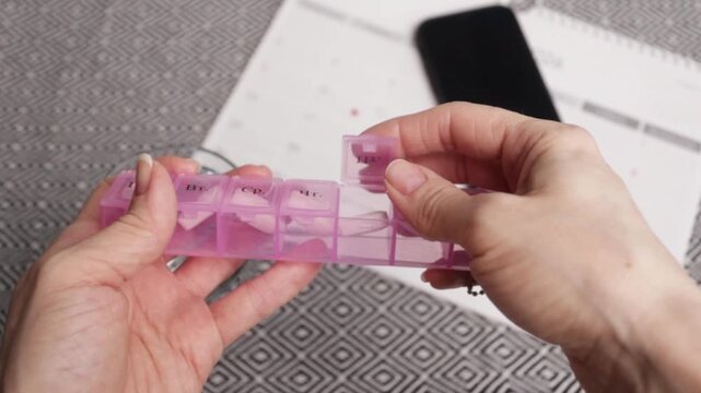 hands place a pill into organizer with smartphone and calendar background, medication planning