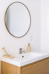 Minimalistic bathroom interior with round mirror, sink and toothbrushes