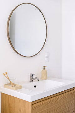 Minimalistic bathroom interior with round mirror, sink and toothbrushes