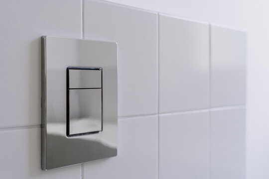 Modern toilet bowl with metal water flush button in clean bathroom