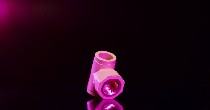 Single pink plastic T-joint pipe fitting with internal metal screw thread on dark background with red light