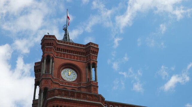 BERLIN, GERMANY - MARCH 23 2026: Static close up of the red brick tower of the Rotes Rathaus (Red Town Hall) featuring the historic clock and the Berlin city flag under a blue sky