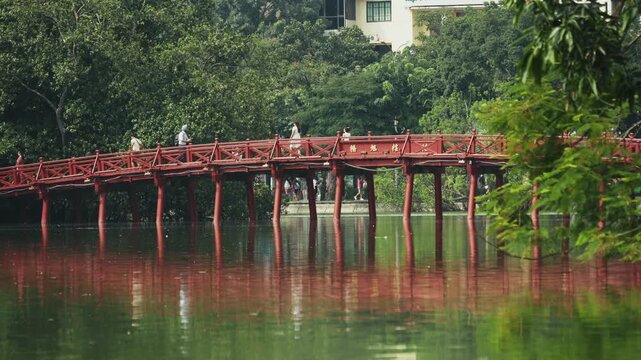People traversing iconic bright red Huc Bridge, historical wooden structure, reflecting vividly