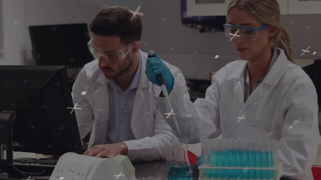 Man at lab computer typing while woman lifting pipette and transferring blue liquid for sample prep