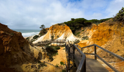 Fototapeta premium Scenic view of cliffs in Portugal with ocean waves and a wooden pathway leading through the rugged landscape.