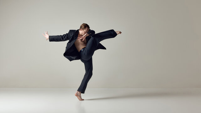 Male dancer executing powerful high kick with dynamic upper body motion in studio. Concept of physical control, flexibility, contemporary choreography and expressive movement in performance art