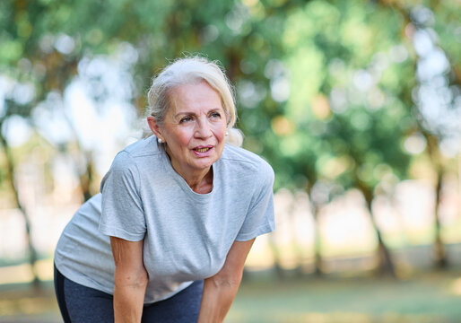 Portrait of a senior elderly woman exercising in a park, tired mature female running and taking a break outdoors, healthy lifestyle and cardio exercise in nature concepts, vitality and active senior