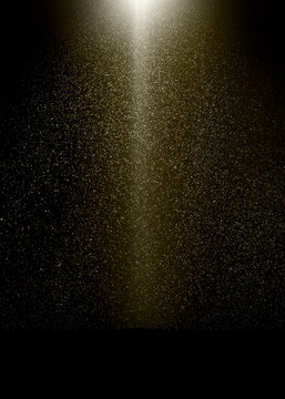 Golden light beam illuminates falling dust particles on a black background