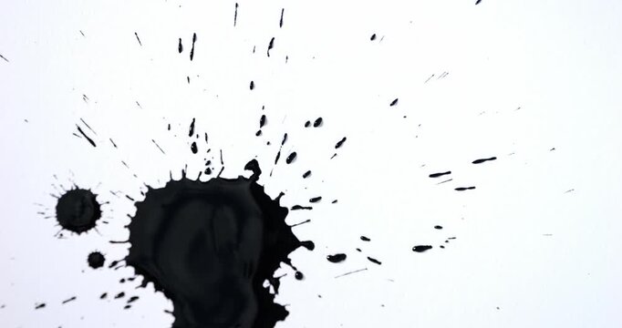 Black spots on a white background. Ink spills onto white paper. Black drops and white surface.