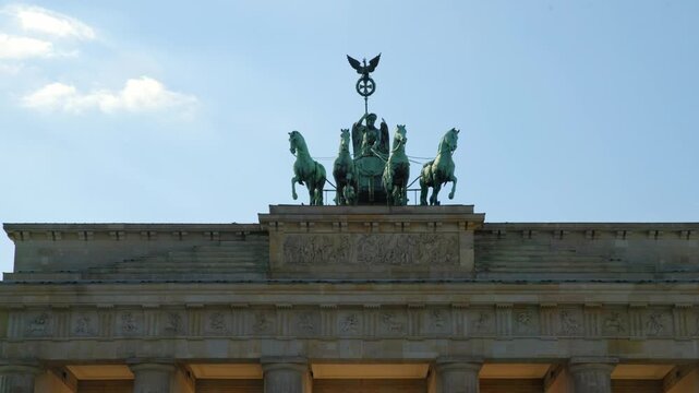BERLIN, GERMANY - MARCH 23 2026: Panning shot close up of the Quadriga statue on top of the Brandenburg Gate with dramatic sunlight and lens flare in the background
