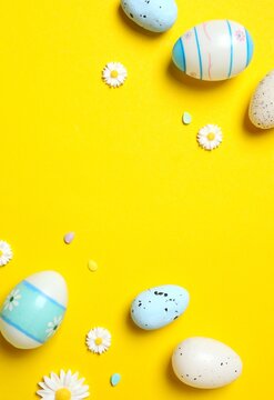 Top vertical view of pastel decorated eggs and small daisies on yellow background, spring celebrations and seasonal decor. Top view