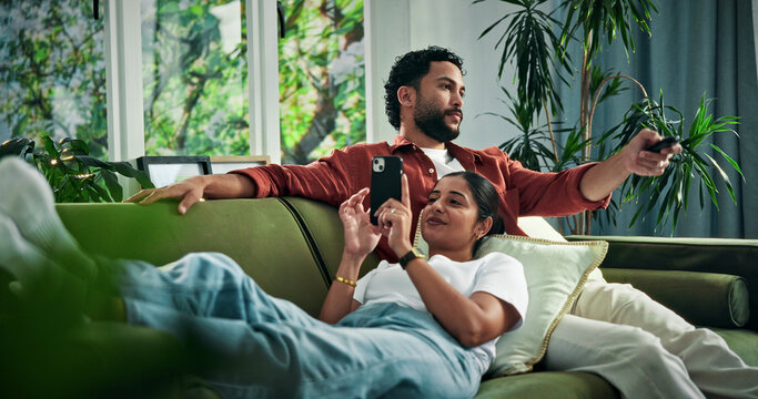 Happy couple, relax and watching tv with phone on sofa for entertainment together in home. Man, woman and online subscription with mobile smartphone or remote on couch for app, movie or news in house