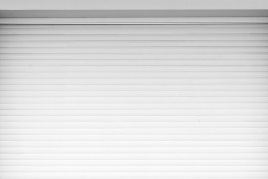 Closed white roller shutter garage door with clean horizontal lines and subtle texture, creating a minimalist architectural background that conveys security, privacy and industrial design