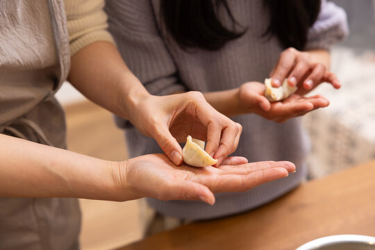 Close-up of a woman and a girl wrapping gyoza dumplings with filling at home