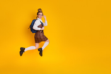 Obraz premium Cheerful teenage student jumping with excitement against a vibrant yellow background wearing a school uniform and backpack