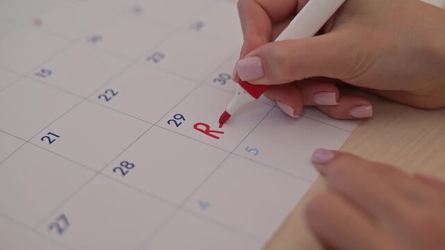 A hand writes the word Rent in red on a calendar date while holding a marker. The action suggests organization and planning related to rental payments
