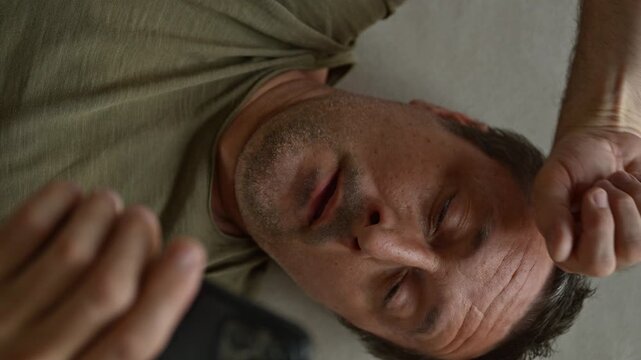 Adult caucasian male laying on the bed and using mobile phone, high angle view, 4K