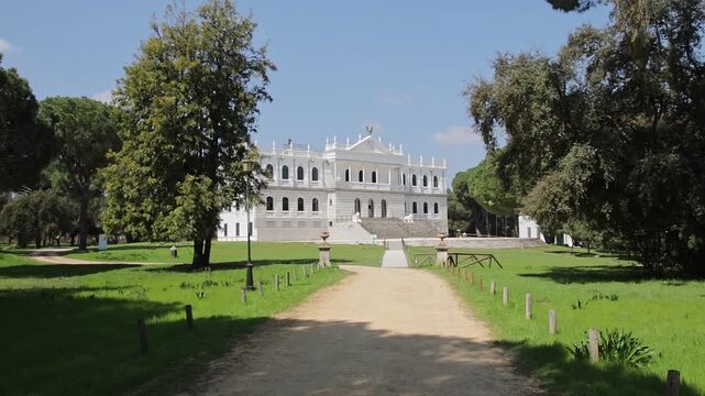 Elegant white facade of Palacio del Acebron surrounded by lush green gardens and a dirt path under a clear blue sky in Almonte, Huelva, Spain.