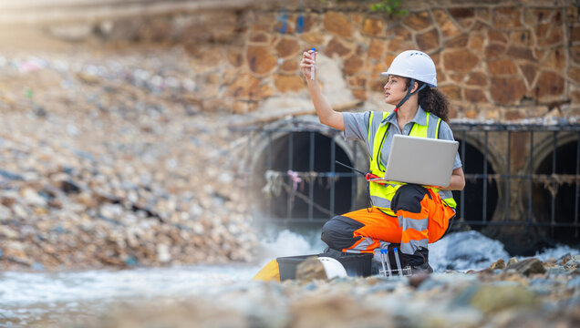 Female Environmental Scientist in Safety Gear Taking Water Samples Near Industrial Drainage, Specialized Technician Inspecting Water Quality with Test Tube and Laptop at Outfall Pipe