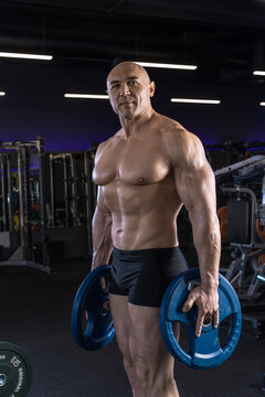 Muscular man poses confidently with weights in a modern gym setting.