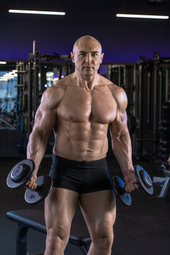 Muscular man holds dumbbells while posing confidently in a gym setting.