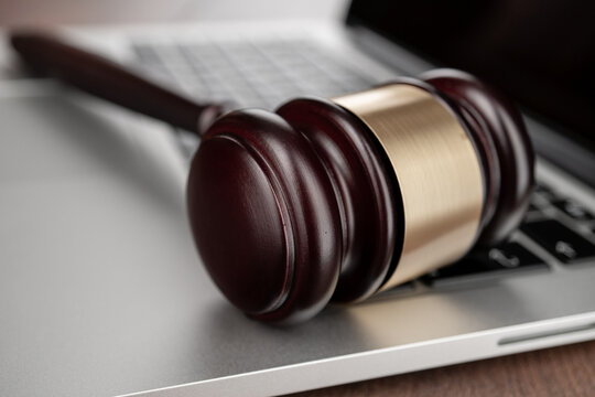 Closeup photo of wooden gavel on modern laptop keyboard, symbolizing themes of legal charges or lawsuit in computer tech industry.