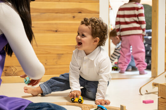 Toddler child playing with toy cars on the floor at kindergarten, laughing happily