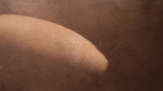Soft oval beam of sunlight moves slowly across the copper surface. Warm copper background for design.