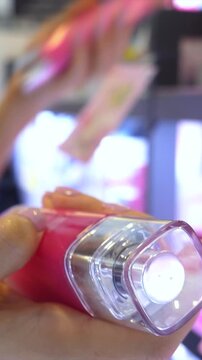Female customer with a beautiful manicure holding a pink bottle of perfume while shopping for new fragrances and beauty products in a bright, modern cosmetics department store