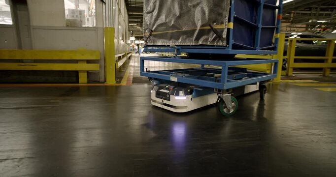 Autonomous mobile robot transporting a heavy blue cargo rack through a large industrial warehouse facility