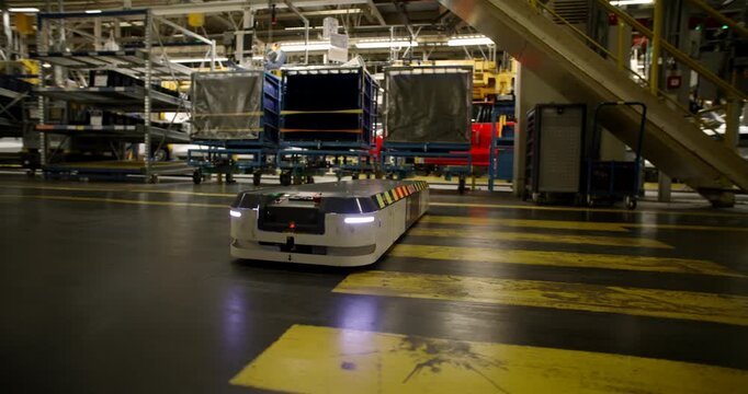 Autonomous mobile robot transporting a heavy blue cargo rack through a large industrial warehouse facility