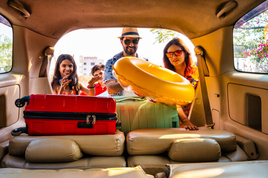 Young Indian family sitting in car as father loads suitcases for a holiday