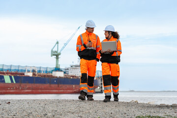 Logistics Supervisors in Safety Uniforms Discussing Operations Near Cargo Ship at Sea Port, Diverse...