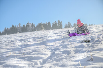A joyful child sledging on a pink sledge, surrounded by a picturesque winter landscape, showing pure delight while enjoying the snow on a bright sunny day