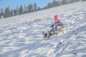 A joyful child sledging on a wooden sledge, surrounded by a picturesque winter landscape, showing pure delight while enjoying the snow on a bright sunny day.
