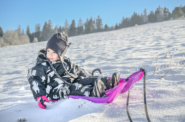 A young child sits relaxed on a bright sled, gazing innocently at the snowy landscape, capturing the essence of childhood wonder and joy in winter