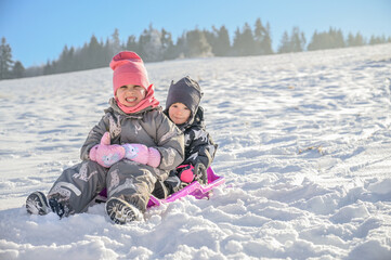 Two siblings experience the joy of winter together as they ride a sled down a snowy hill, creating lasting memories filled with excitement and happiness