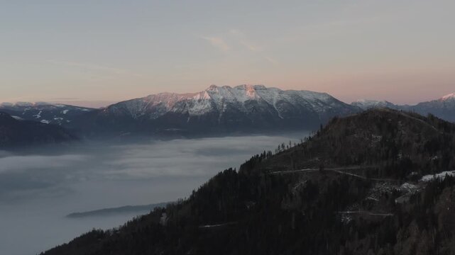 Drone 4K aerial view of Cima Vigolana mountain peak at sunrise with alpenglow and sea of clouds. Pink dawn light over Alps, Valsugana, Levico Terme, Trentino, Italy