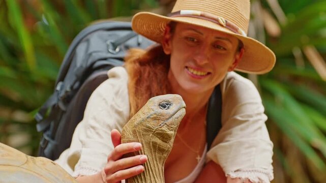 Woman in hat pet the head of a rare, giant turtle on the tropical island of Mauritius