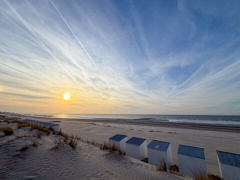 Colorful beach huts at sunset on Nieuwpoort beach, Belgium with dramatic sky and golden light reflecting on ocean waves