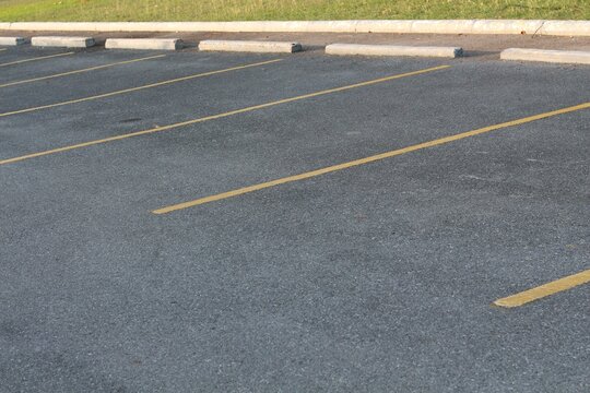 Empty asphalt parking lot with yellow lines and concrete curbs on a sunny day