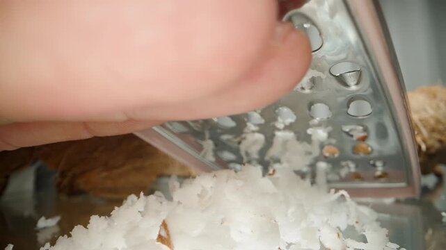 Man's Hand Collecting Freshly Grated Coconut Shavings from Under the Metal Grater, Macro View.