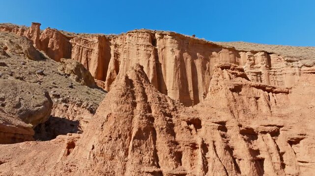 Aerial view reveals stunning geological formations in Kyrgyzstan's badlands. Rugged canyons and layered rocks showcase natural beauty under sunny skies.