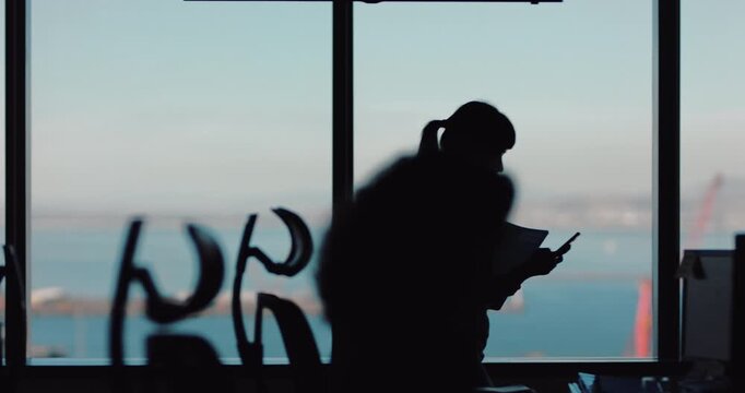 Woman, phone and texting with silhouette by window, walk and notification in office at insurance company. Person, smartphone and broker in corridor on mobile app, contact and web chat at agency