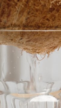 Vertical video. Turning a coconut with a hole upside down and placing it on a glass to drain the sweet milk. Close-up.