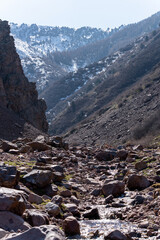 Obraz premium A rugged mountain valley view with steep, rocky slopes leading to a snow-dusted background. The foreground is dominated by large boulders and sparse green vegetation, suggesting a spring season.
