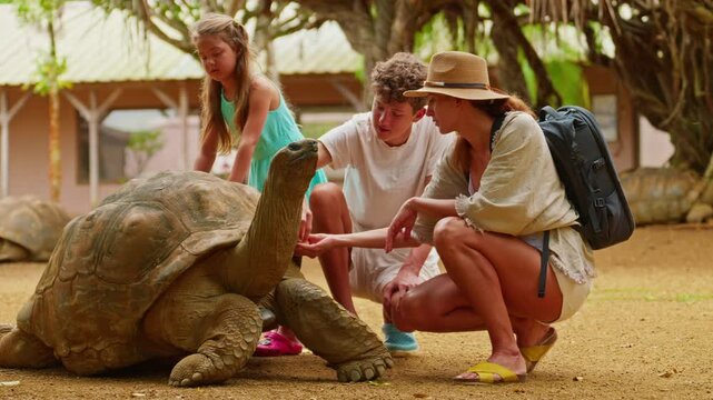 Family pet the head of a rare, giant turtle on the tropical island of Mauritius