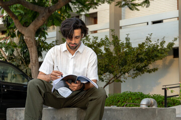 Fototapeta premium Young Latino man writing notes in a notebook in an urban outdoor setting.